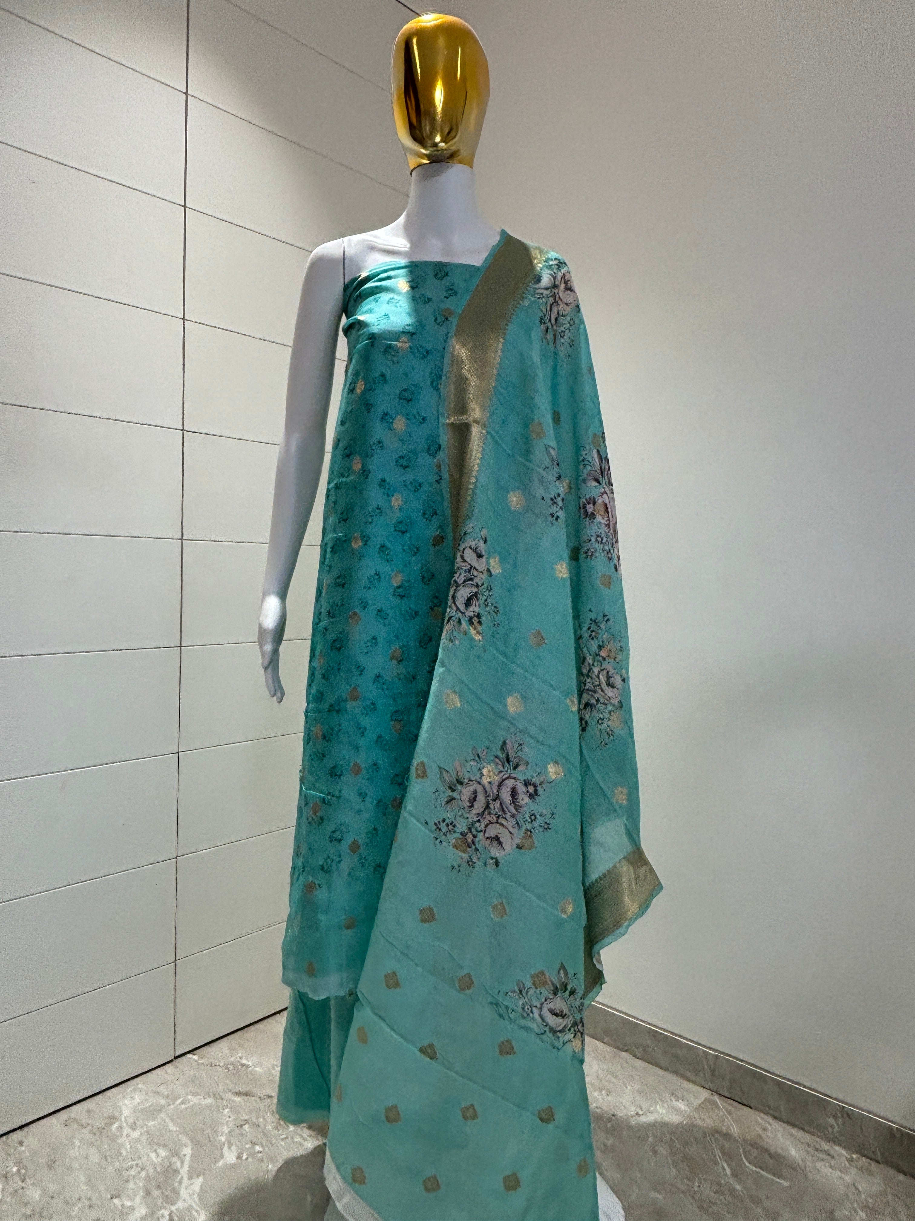 A sea blue colored Banarasi silk suit material displayed on a mannequin, featuring floral embroidery and a golden border.